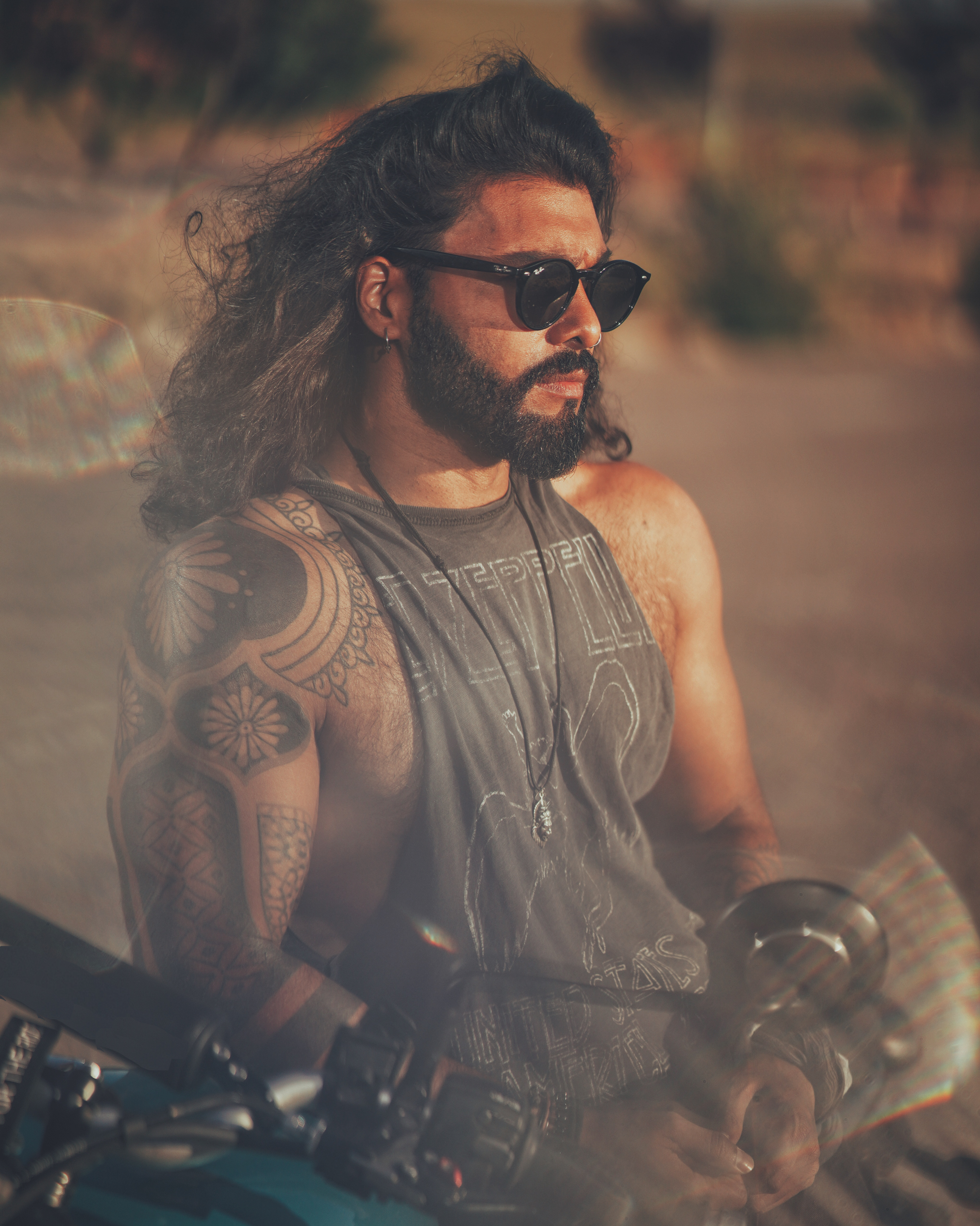 Man with tattoos and sunglasses sitting on a motorcycle in a desert setting